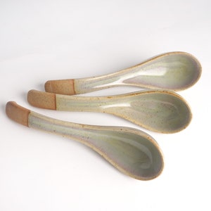 May include: Three ceramic soup spoons with a light green glaze and brown handles.
