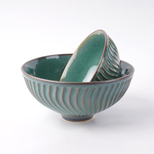 May include: Two teal ceramic bowls with a wavy, textured design. The smaller bowl is nested inside the larger bowl.