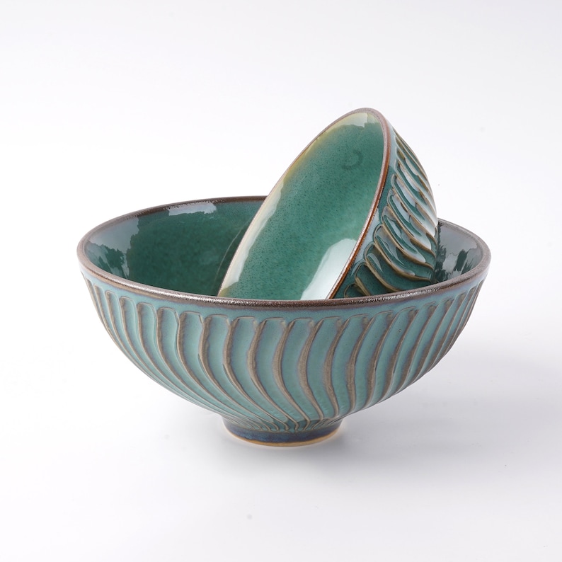 May include: Two teal ceramic bowls with a wavy, textured design. The smaller bowl is nested inside the larger bowl.