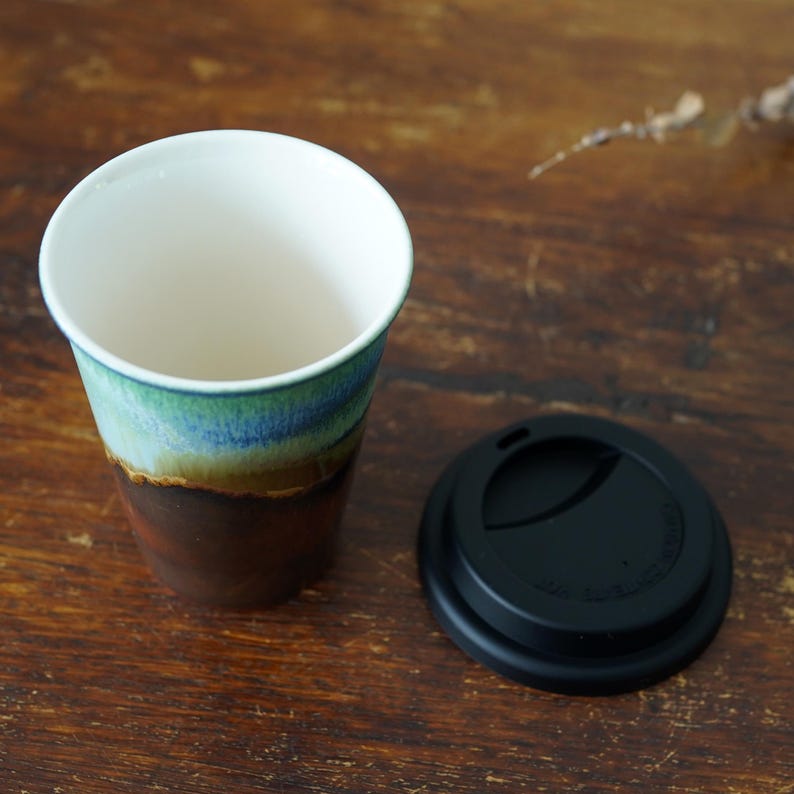 May include: A ceramic travel mug with a brown, green, and blue glaze. The mug has a black lid with a silicone seal.