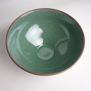 May include: A green ceramic bowl with a brown rim. The bowl has a speckled glaze and a glossy finish.