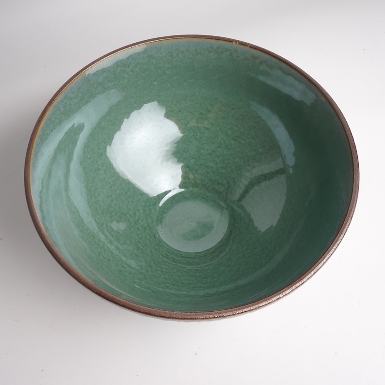 May include: A green ceramic bowl with a brown rim. The bowl has a speckled glaze and a glossy finish.