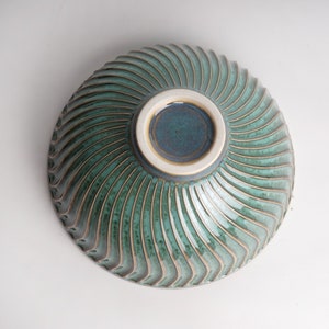 May include: A green ceramic bowl with a swirling, textured design. The bowl has a white rim and a dark green interior.
