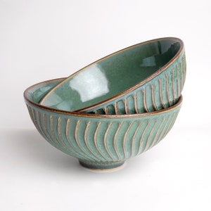 May include: Two green ceramic bowls with a brown rim and a wavy pattern. The bowls are stacked on top of each other.