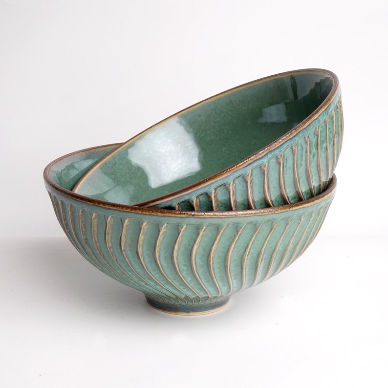 May include: Two green ceramic bowls with a brown rim and a wavy pattern. The bowls are stacked on top of each other.