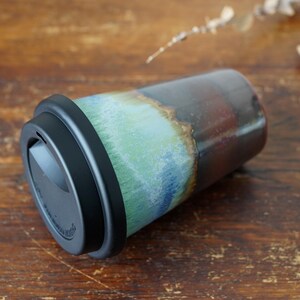 May include: A ceramic travel mug with a black lid. The mug has a blue, green, and brown glaze with a layered effect.