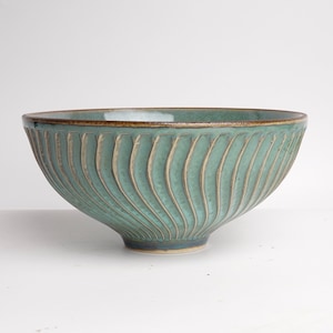 May include: A large, teal ceramic bowl with a wavy, ribbed design. The bowl has a brown rim and a slightly flared base.
