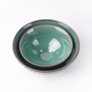 May include: Two green ceramic bowls, one nested inside the other. The larger bowl has a textured rim and the smaller bowl has a smooth rim.