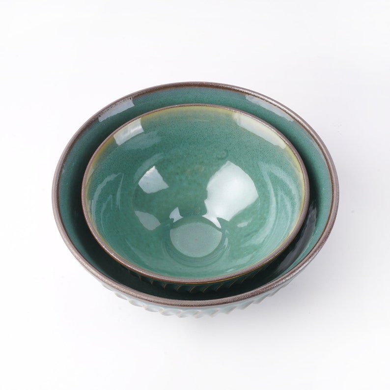 May include: Two green ceramic bowls, one nested inside the other. The larger bowl has a textured rim and the smaller bowl has a smooth rim.