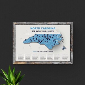 May include: A framed map of North Carolina with a blue outline of the state and black dots marking the locations of the top 50 disc golf courses. The title of the map reads "North Carolina Top 50 Disc Golf Courses".