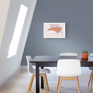May include: A framed map of North Carolina highlighting the top 50 golf courses in the state. The map is printed on white paper with a light orange outline of the state and red dots marking the golf courses. The title "North Carolina Top 50 Golf Courses" is printed in red at the top of the map.