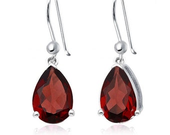 Puede incluir: Un par de pendientes colgantes de plata con piedras preciosas rojas en forma de pera y facetadas. Los pendientes tienen un diseño sencillo con cierre de gancho y una pequeña bola de plata en la parte superior.