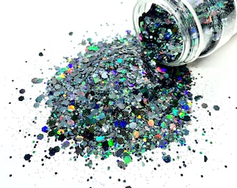 May include: A glass jar filled with iridescent black glitter, spilling out onto a white surface. The glitter is a mix of different sizes and shapes, with a rainbow of colors shimmering through the black.