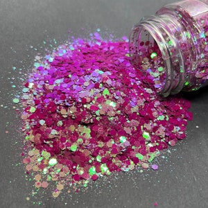 May include: A clear jar with a pink, green, and white iridescent glitter mix spilling out onto a dark grey surface.