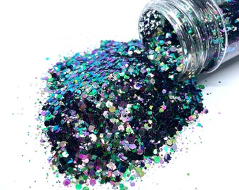May include: A clear plastic jar filled with iridescent glitter in shades of green, black, and purple. The glitter is spilling out of the jar onto a white surface.
