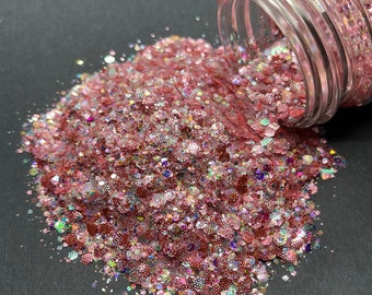 May include: A pink and iridescent glitter mix pours out of a clear glass jar onto a black surface. The glitter is a mix of different sizes and shapes, with some pieces being larger and more chunky than others.
