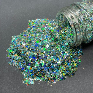 May include: A jar of green, blue, gold, and iridescent glitter. The glitter is spilling out of the jar onto a black surface.