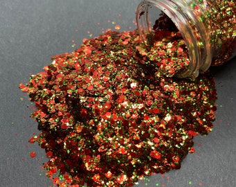 May include: A jar of red, green, and gold glitter spills out onto a gray surface. The glitter is a mix of different sizes and shapes.