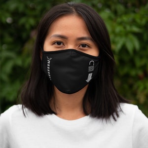 May include: Black face mask with a zipper design on the left side and a lock and arrow graphic on the right. The mask is made of a soft material and is designed to cover the nose and mouth.
