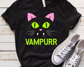 May include: Black t-shirt with a neon green and pink cat face graphic and the text "Vampurr" in neon green.