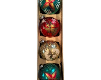Könnte beinhalten: Ein Set aus vier runden Weihnachtskugeln aus Glas, die vertikal in einem Karton angeordnet sind. Die obere und untere Kugel sind grün mit einem roten und goldenen Sternmuster. Die zweite ist rot mit einem goldenen Engel und die dritte ist gold mit Glitzer.