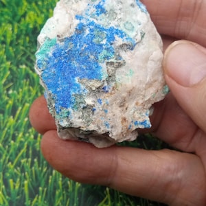 May include: A raw mineral specimen featuring a rough, irregular shape with a white base matrix. The surface is heavily textured with vibrant patches of deep blue azurite and bright green malachite deposits, interspersed with small metallic flecks.