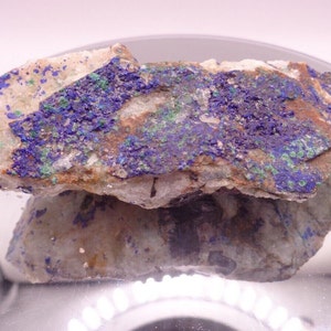May include: A rough, natural rock specimen with a mix of blue, green, and brown colors. The rock has a rough, uneven surface and appears to be a combination of different minerals.