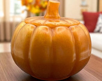 Puede incluir: Un tarro decorativo con forma de calabaza de color naranja con tapa. El tarro tiene un acabado brillante y está sobre una superficie de madera. La calabaza tiene un tallo en la parte superior y está diseñada con surcos verticales.
