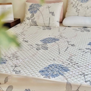 May include: A bed with a floral patterned comforter and matching pillows. The comforter and pillows feature a white background with large blue flower and gray leaf designs. The bed skirt also has a floral pattern. The text "Ảnh chụp thật" is visible.