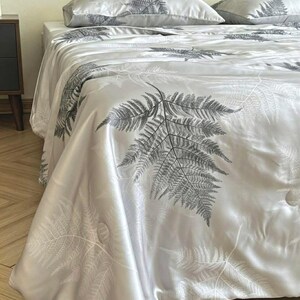 Peut inclure: Un couvre-lit gris clair et des taies d'oreiller assorties orn&eacute;s d'un motif de feuilles de foug&egrave;re gris fonc&eacute;. La parure de lit pr&eacute;sente une finition satin&eacute;e lisse avec des d&eacute;tails de surpiq&ucirc;res circulaires sur le tissu.