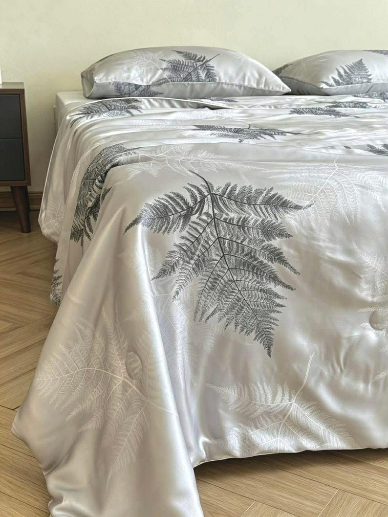 Peut inclure: Un couvre-lit gris clair et des taies d'oreiller assorties orn&eacute;s d'un motif de feuilles de foug&egrave;re gris fonc&eacute;. La parure de lit pr&eacute;sente une finition satin&eacute;e lisse avec des d&eacute;tails de surpiq&ucirc;res circulaires sur le tissu.