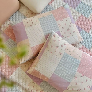 May include: Two rectangular patchwork pillows with a floral and plaid pattern in pastel shades of pink, lavender, and light blue. The pillows rest on a matching patchwork quilt.