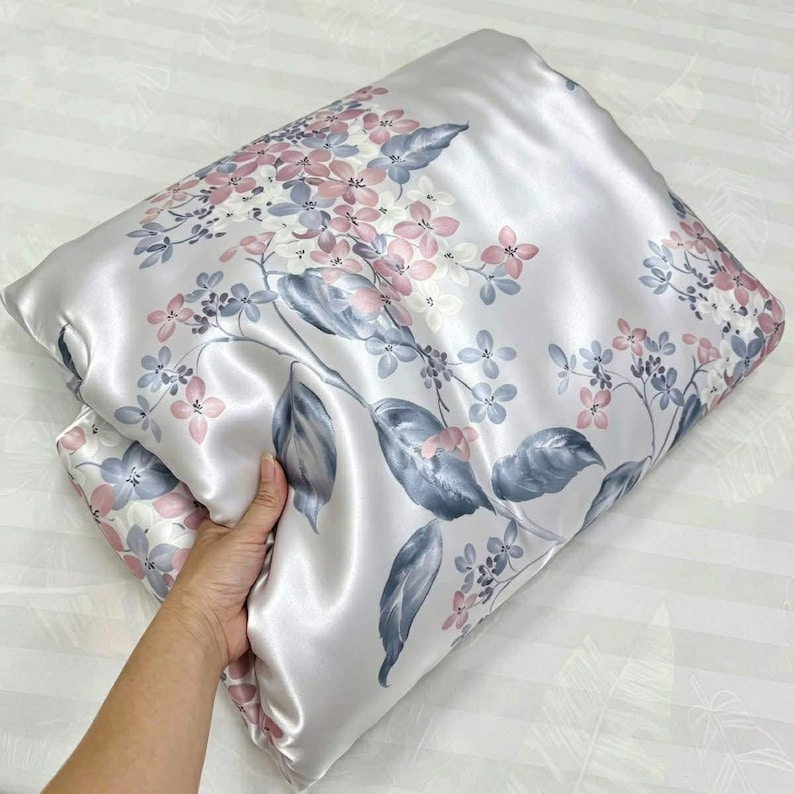 Peut inclure: Une taie d'oreiller rectangulaire en tissu lisse et brillant gris clair, orn&eacute;e d'un motif imprim&eacute; de grappes de fleurs d&eacute;licates dans des tons rose tendre, bleu sourd et blanc, avec des feuilles gris fonc&eacute; et des tiges fines.