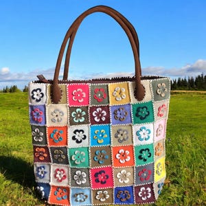 May include: A patchwork tote bag with a brown leather handle and a zipper closure. The bag is made of different colored squares of fabric, each with a flower design.