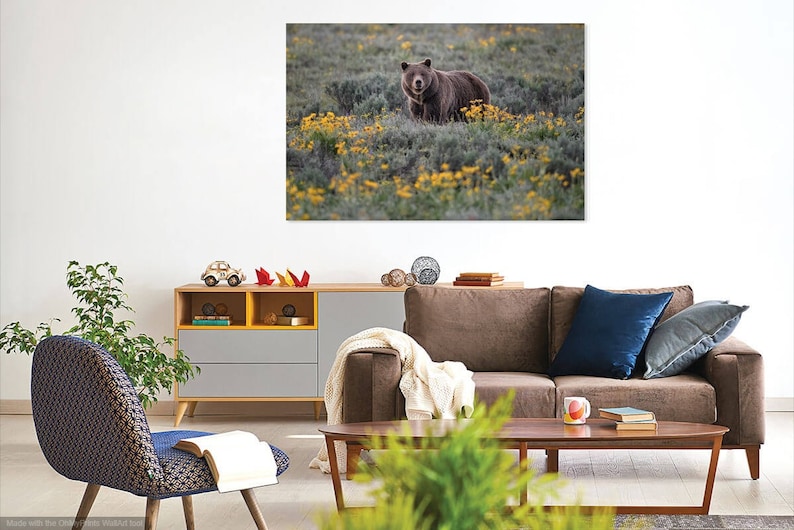 May include: A framed canvas print featuring a brown bear in a field of yellow wildflowers. The bear is centered in the image, surrounded by green foliage and blooms. The artwork is displayed above a modern living room setup.