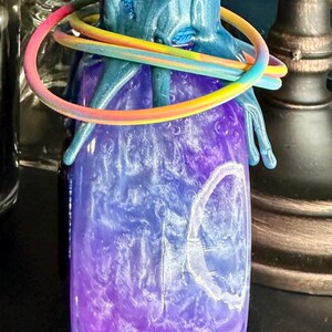 Puede incluir: Un tarro decorativo con un dise&ntilde;o degradado azul y morado. El tarro tiene una parte superior azul texturizada con un anillo de color arco&iacute;ris alrededor del cuello. El cuerpo del tarro tiene un efecto arremolinado y veteado.