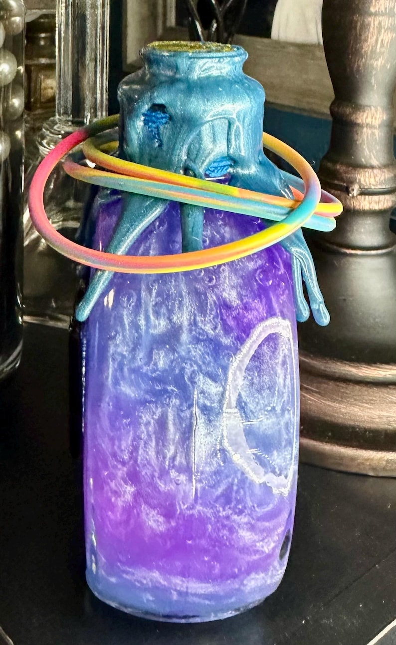 Puede incluir: Un tarro decorativo con un dise&ntilde;o degradado azul y morado. El tarro tiene una parte superior azul texturizada con un anillo de color arco&iacute;ris alrededor del cuello. El cuerpo del tarro tiene un efecto arremolinado y veteado.