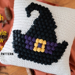 May include: A crocheted pillow cover featuring a witch hat design with black, purple, and yellow bobbles. The pillow cover is made with a white yarn and has a textured surface. "CROCHET PATTERN" is written in the bottom left corner.