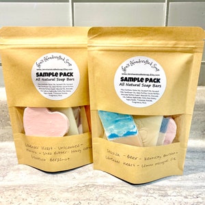 May include: Two brown paper bags with a sample pack of all-natural soap bars. The bags are labeled with the text "Gen's Handcrafted Soap" and "Sample Pack". The soap bars are in various shapes and colors, including lavender heart, seaside, and Kentucky bourbon.