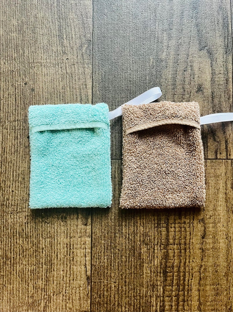 Puede incluir: Dos esponjas de ba&ntilde;o, una azul claro y otra marr&oacute;n, con cordones blancos. Las esponjas est&aacute;n hechas de un tejido suave y texturizado.