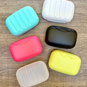 May include: Six soap dishes in various colors, including white, light blue, black, pink, yellow, and clear. The dishes are made of plastic and have a ribbed design.