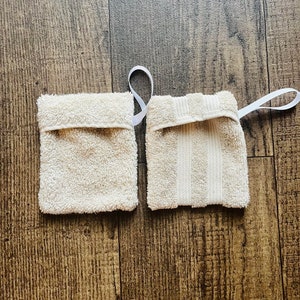 Puede incluir: Dos toallitas de algod&oacute;n blanco con lazos de cinta blanca. Una toallita tiene una superficie texturizada y la otra tiene un patr&oacute;n a rayas.