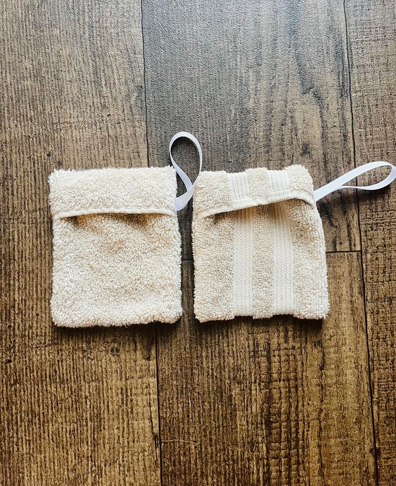Puede incluir: Dos toallitas de algod&oacute;n blanco con lazos de cinta blanca. Una toallita tiene una superficie texturizada y la otra tiene un patr&oacute;n a rayas.