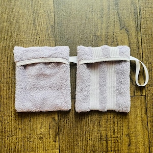 Puede incluir: Dos pa&ntilde;os de lavar de color lavanda con ribete blanco. Un pa&ntilde;o de lavar tiene un patr&oacute;n de rayas y el otro es liso. Ambos pa&ntilde;os de lavar tienen un lazo blanco para colgar.