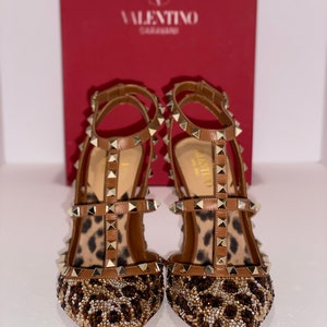 May include: A pair of brown leather high-heeled shoes with gold studs and a leopard print design. The shoes are embellished with small beads and sequins.