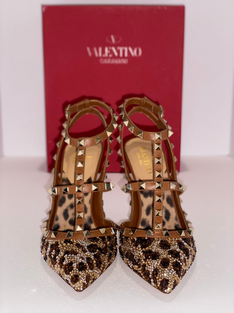 May include: A pair of brown leather high-heeled shoes with gold studs and a leopard print design. The shoes are embellished with small beads and sequins.