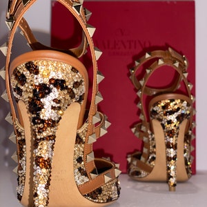 May include: A pair of brown leather high-heeled shoes with gold studs and a leopard print design. The shoes are covered in rhinestones and have a pointed toe.