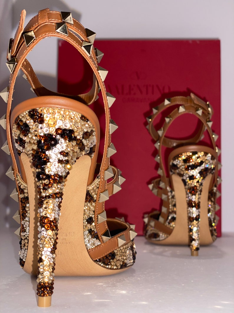May include: A pair of brown leather high-heeled shoes with gold studs and a leopard print design. The shoes are covered in rhinestones and have a pointed toe.