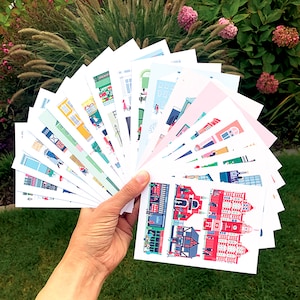 May include: A collection of colourful illustrated postcards featuring various buildings and scenes. The postcards are fanned out in a hand, showcasing the different designs.