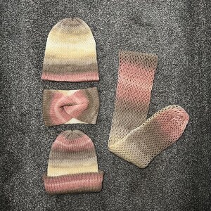 Peut inclure: Un ensemble de trois articles tricotés dans des tons de rose, marron et beige. L'ensemble comprend un bonnet, un bandeau et une longue écharpe.
